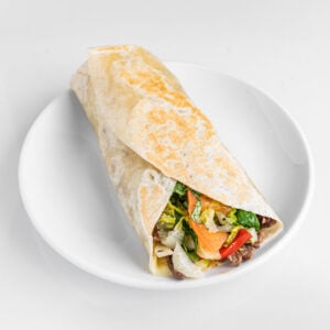 Wrap au steak avec provolone, sauce maison, poivrons r&ocirc;tis, oignons caram&eacute;lis&eacute;s, aubergines, laitue et tomate